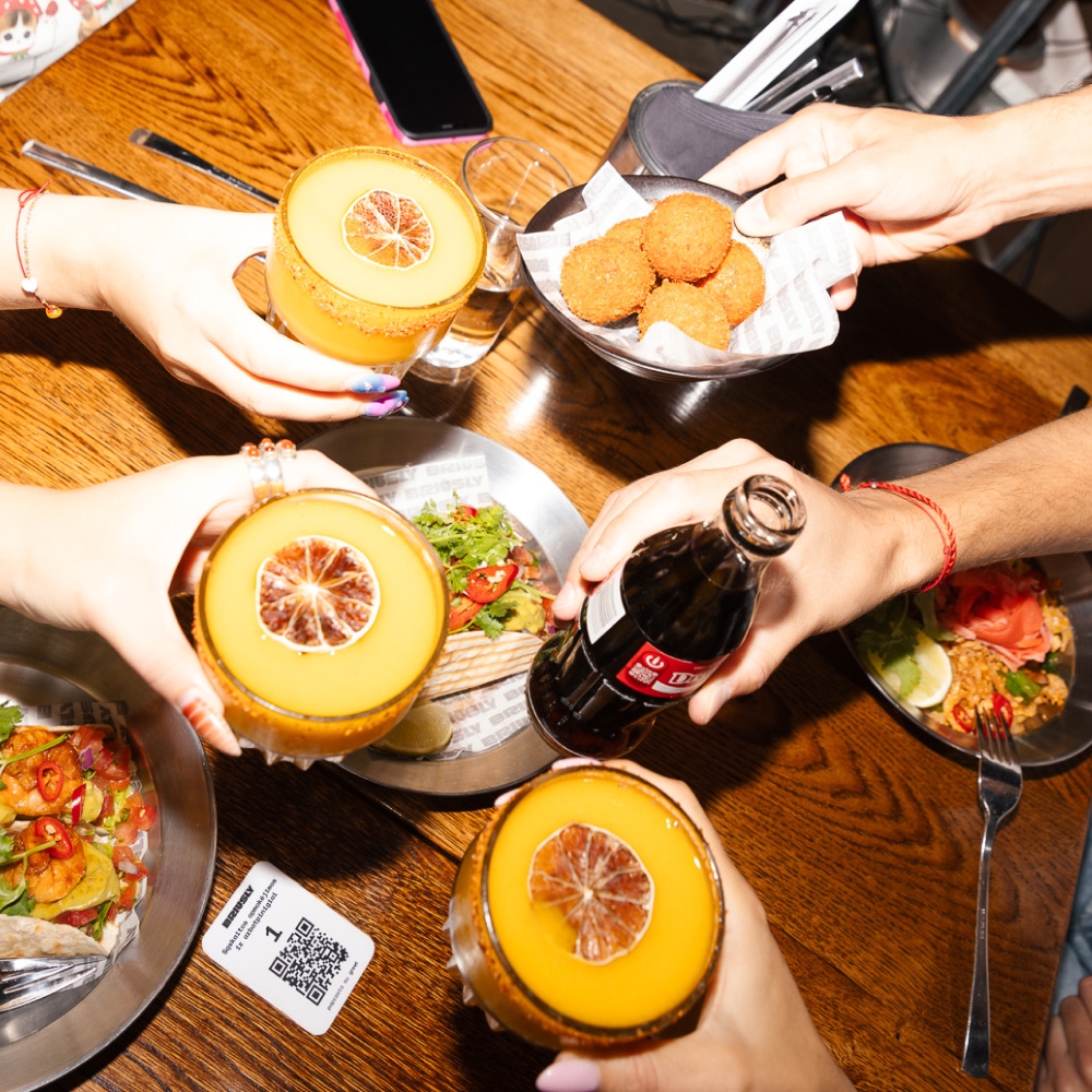 Friends enjoying cocktails, tacos, and snacks at a restaurant table